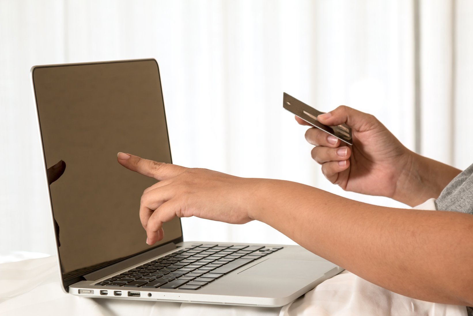 Asian woman pointing at laptop display to confirm credit card information before confirming online shopping